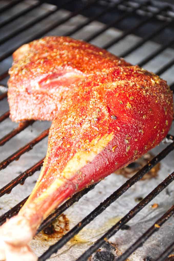 Wild turkey leg rubbed with cajun seasoning rub being smoked on grill grates