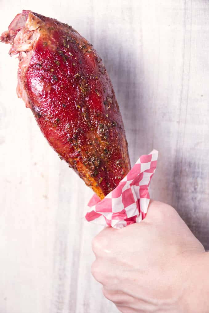 Smoked wild turkey leg being held with a red and white checkered deli paper