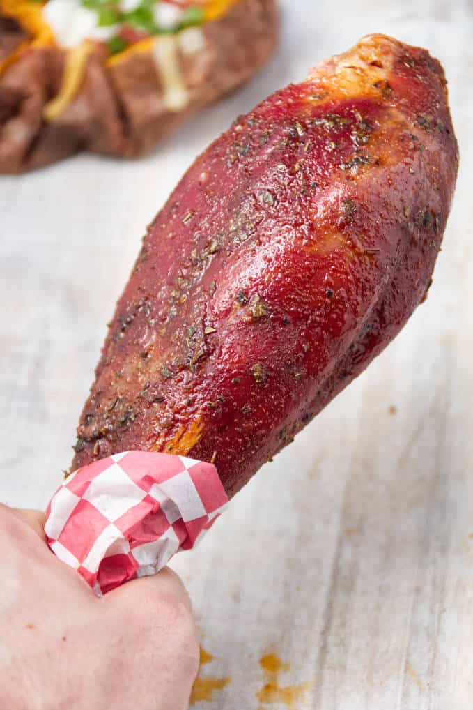 Smoked wild turkey leg laying on white cutting board with loaded baked sweet potatoes