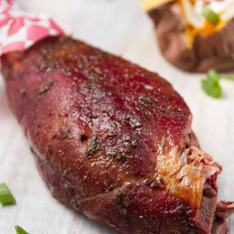 Smoked wild turkey leg laying on white cutting board with loaded baked sweet potatoes and some fried green beans