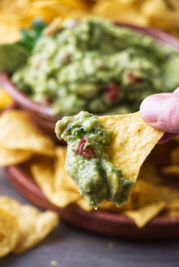 A corn chip dipped in guacamole with tomatoes.