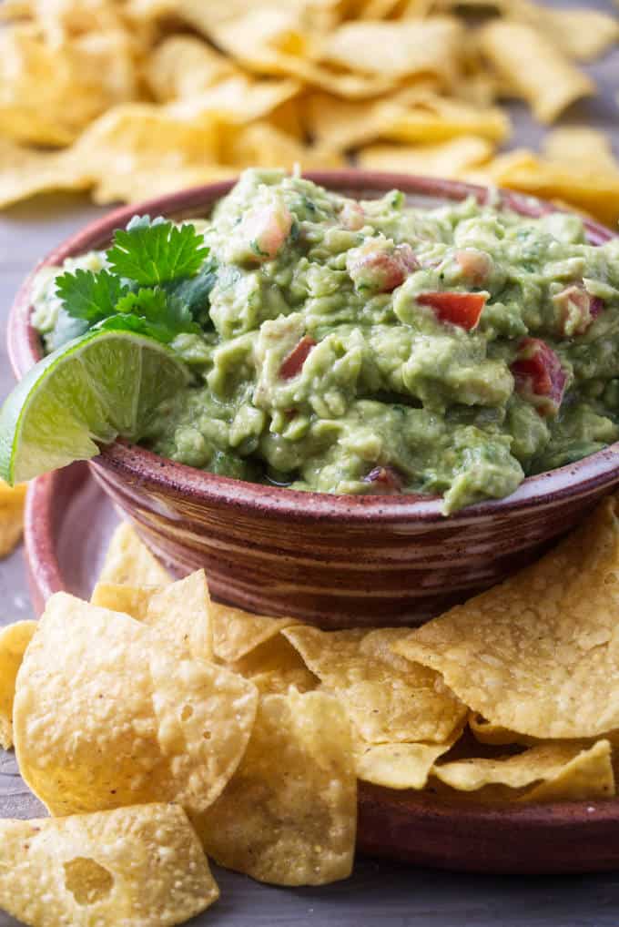 a serving dish of guacamole surrounded by corn chips.