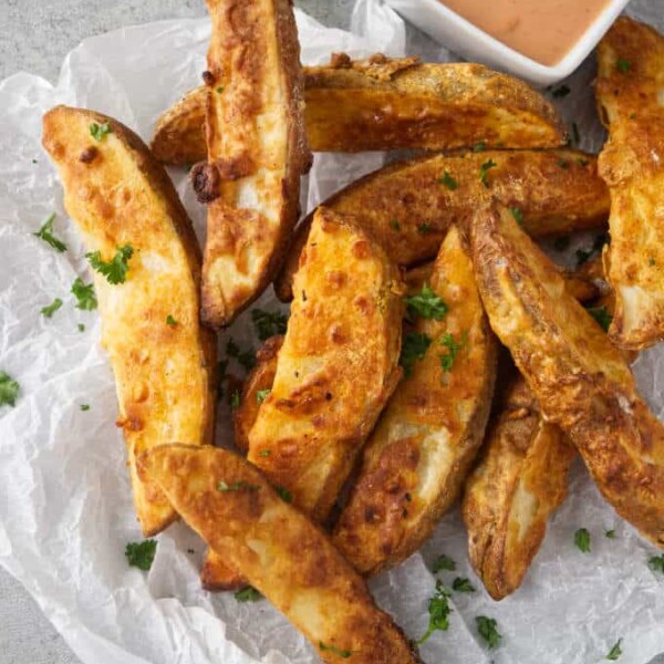 A pile of air fryer potato wedges with a dish of dipping sauce.