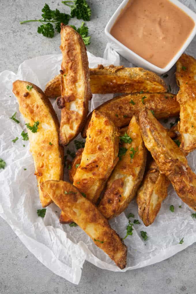 A pile of air fryer potato wedges with a dish of dipping sauce.