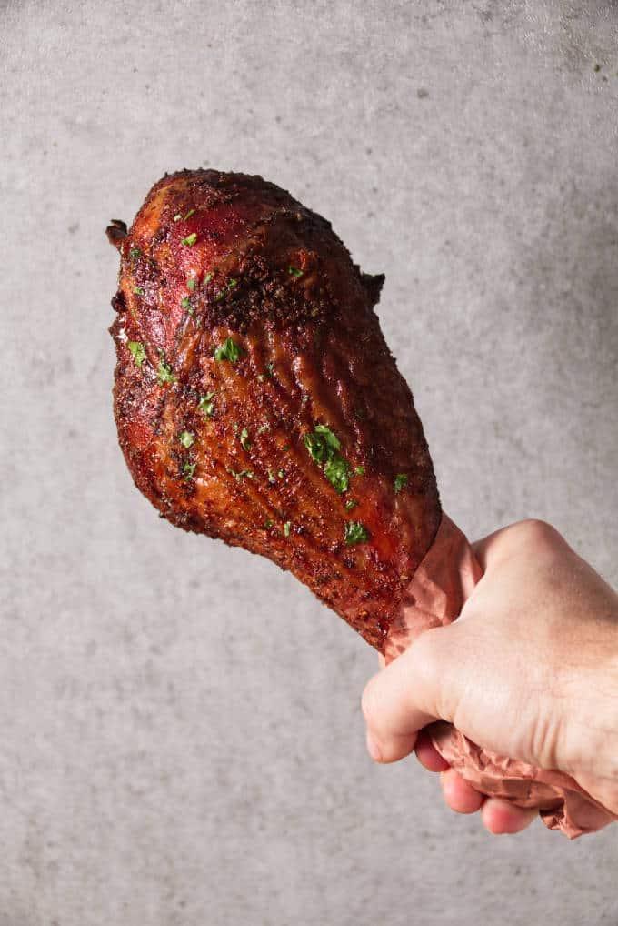 Hand holding a smoked turkey leg with concrete background