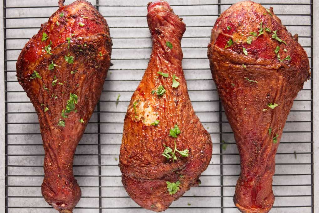 Three smoked turkey legs laying on a metal wire rack to rest