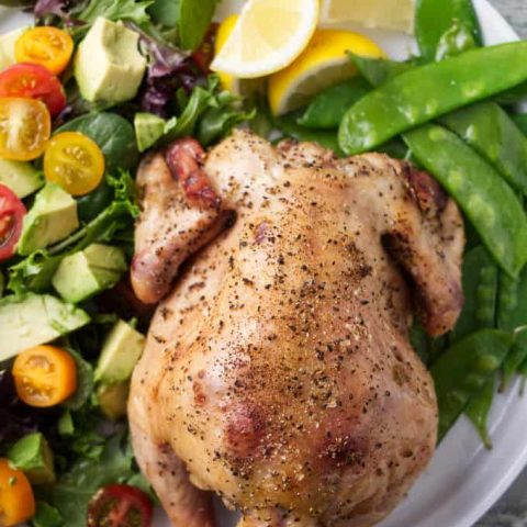 A smoked Cornish game hen on a plate with peas and salad.
