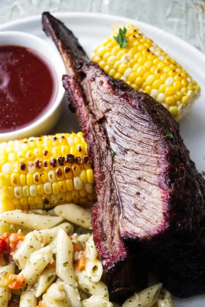 A Dino beef rib on a plate with corn and pasta salad.