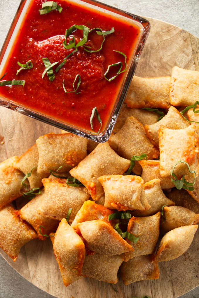 Pizza rolls stacked on wood cutting board with pizza sauce for dipping.