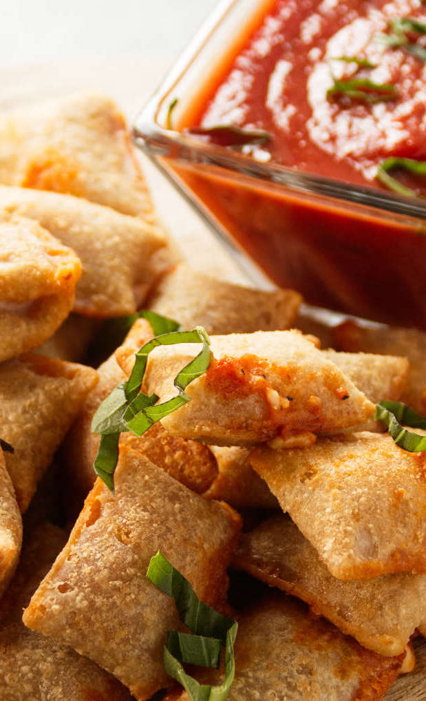 Close up of pizza rolls stacked on wood cutting board with pizza sauce for dipping.