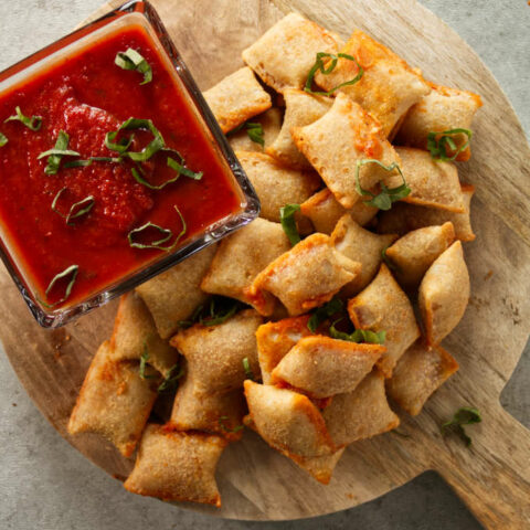 Overhead of pizza rolls stacked on wood cutting board with pizza sauce for dipping.