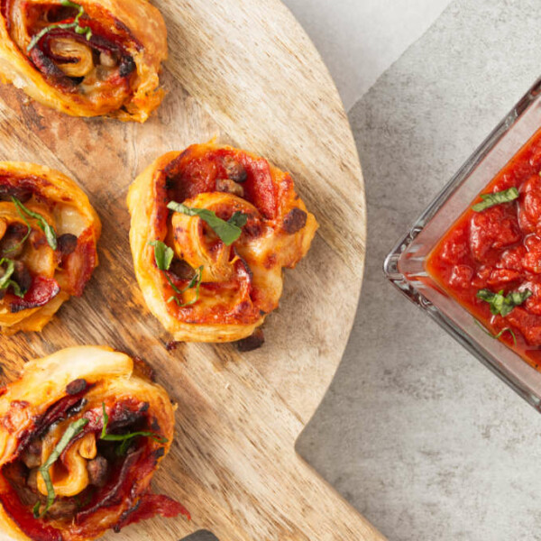 Crispy air fryer pizza rolls on cutting board with pizza sauce in bowl for dipping.