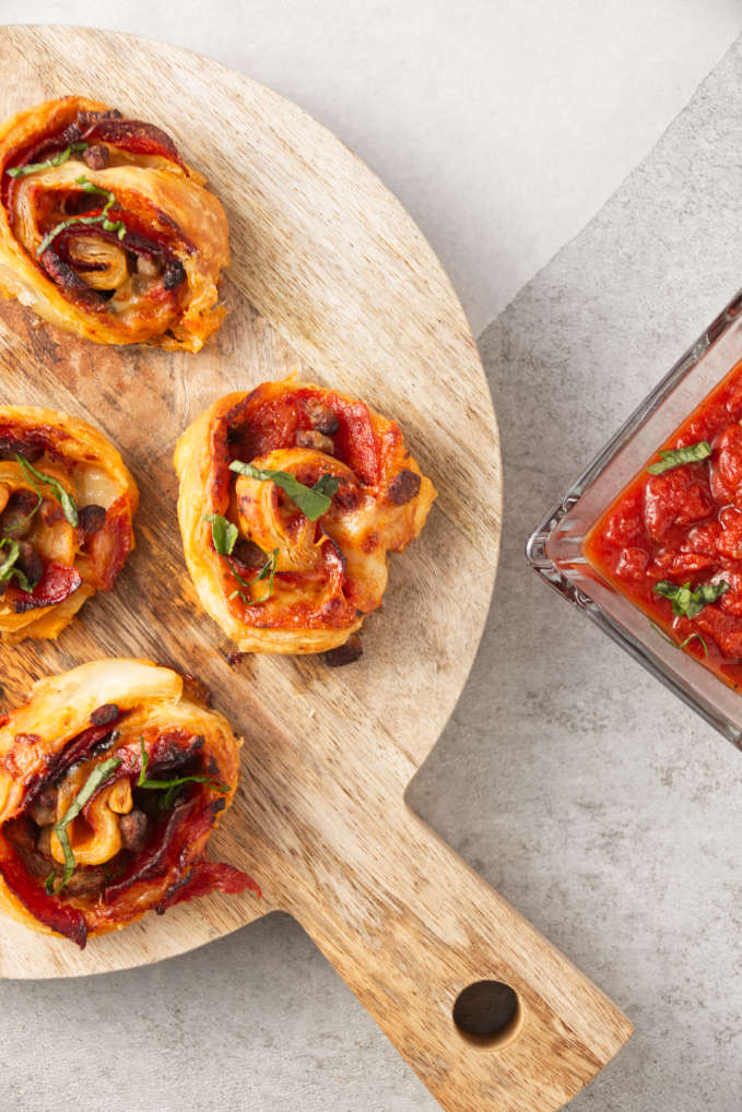 Crispy air fryer pizza rolls on cutting board with pizza sauce in bowl for dipping.