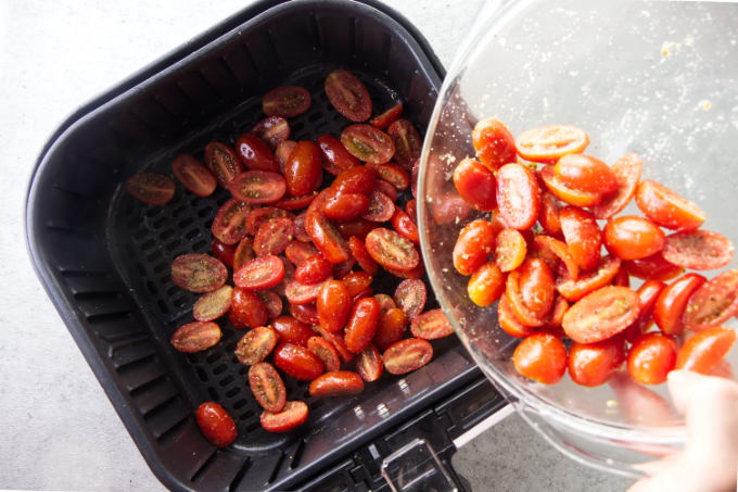 Tossing cherry tomatoes in an air fryer basket.