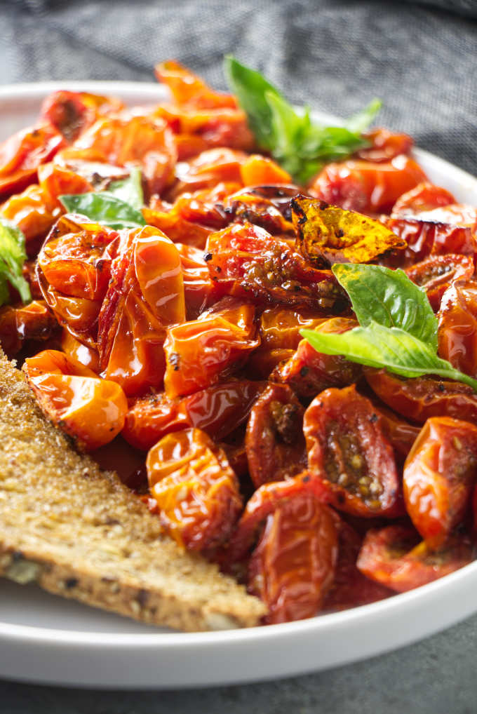 Air fryer cherry tomatoes on a plate with basil garnish.