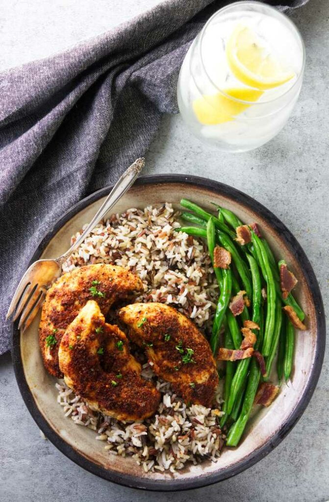 A serving of chicken tenders on a plate with rice and green beans.