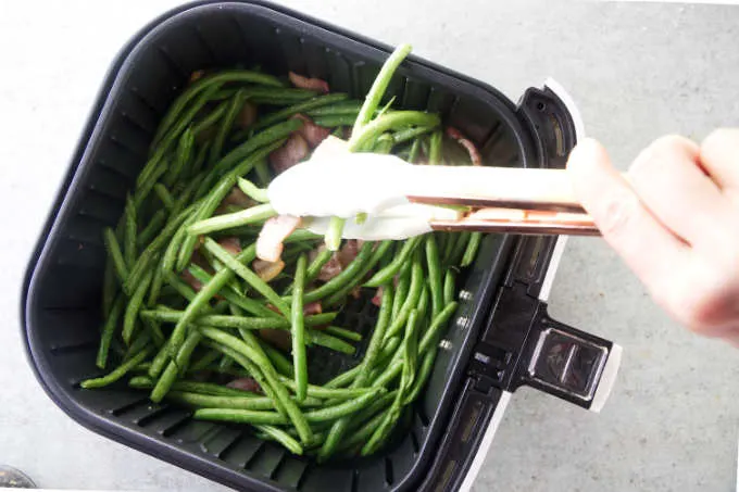 Stirring green beans in an air fryer.