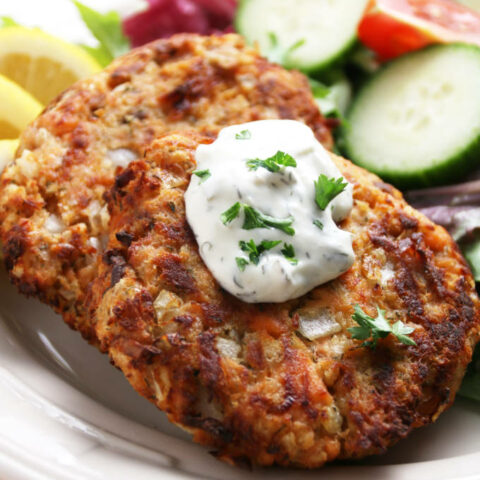 salmon cakes cooked golden brown with dollop of tarter sauce on top with a garden salad