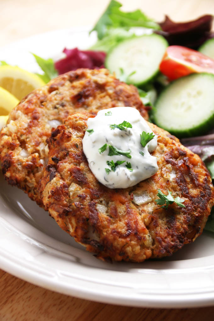 salmon cakes cooked golden brown with dollop of tarter sauce on top with a garden salad