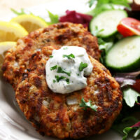 salmon patties cooked golden brown with dollop of tarter sauce on top with a garden salad