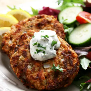 salmon patties cooked golden brown with dollop of tarter sauce on top with a garden salad