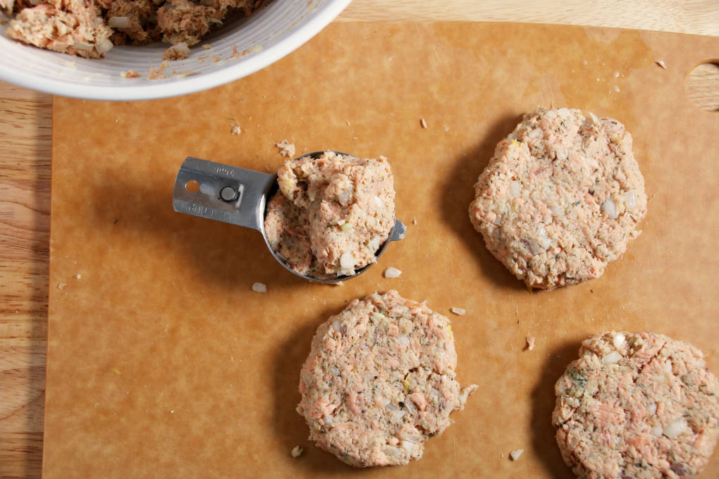 Air fryer salmon patty mixture being formed into patties with a measuring cup.