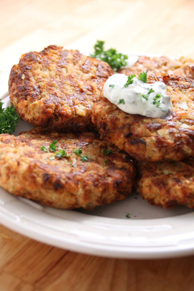 Salmon patties cooked to a golden brown with dollop of tarter sauce on top, stacked on a plate.