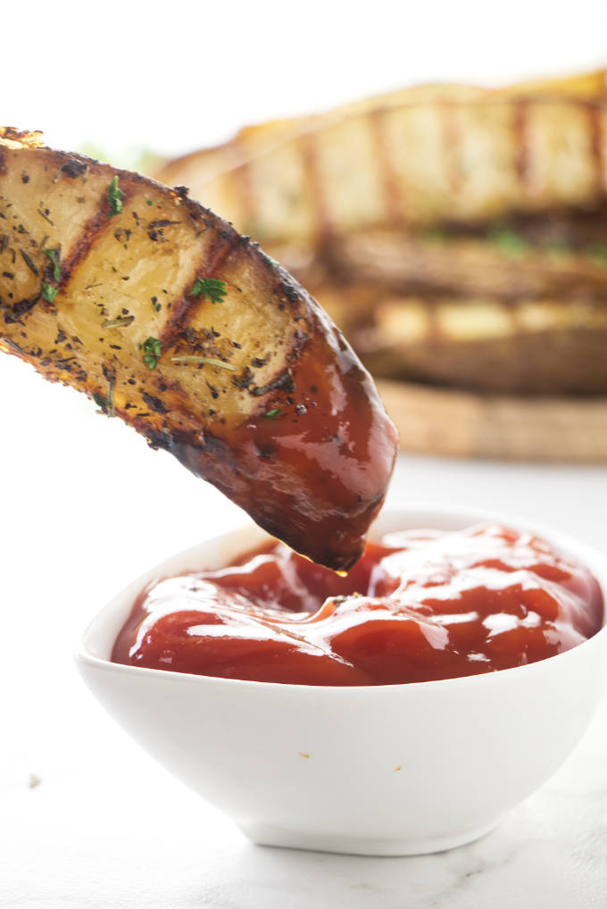 Grilled potatoes being dipped into ketchup.