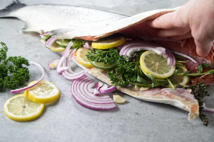 Stuffing a whole salmon with lemon, onion, garlic, and herbs.