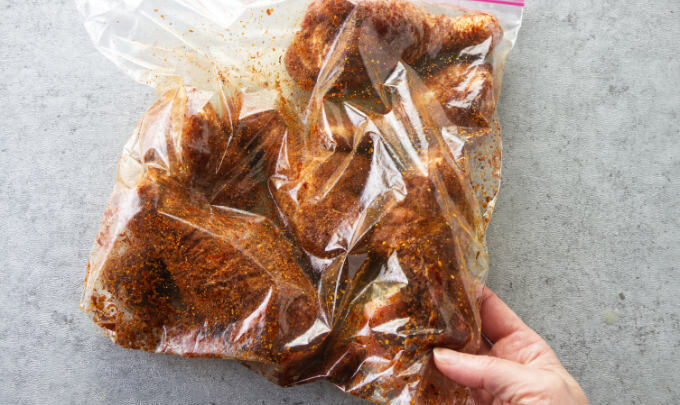 Chicken legs in a plastic bag with bbq dry rub seasoning.