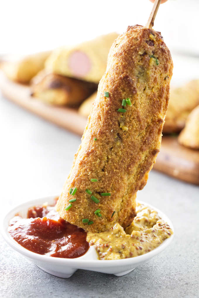 A corn dog being dipped into ketchup.