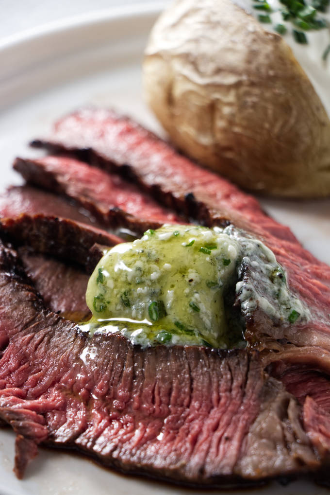 Slices of grilled chuck roast on a plate with a baked potato.