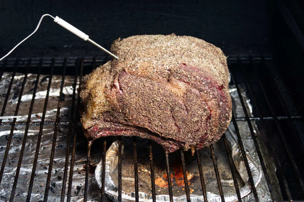 Prime rib with thermometer stuck in it, resting on the Traeger grill grates.