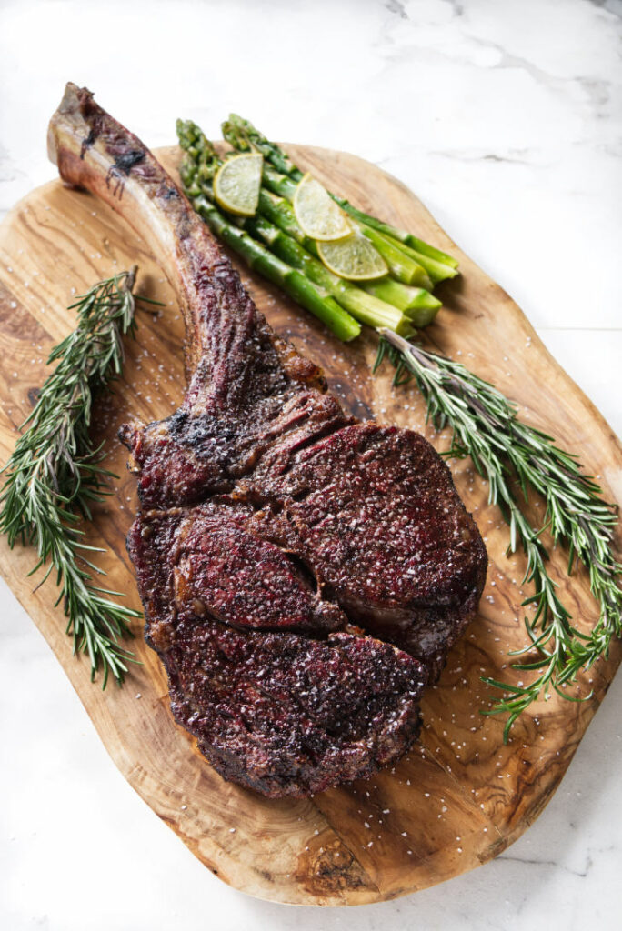 seared tomahawk steak being held vertically from the bone, resting on cutting board