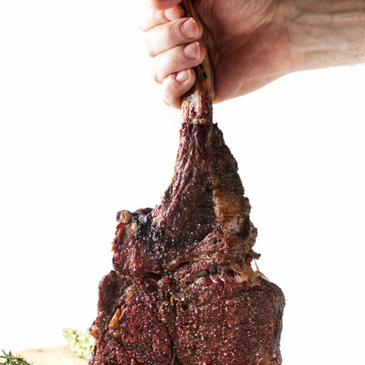 seared tomahawk steak being held vertically from the bone, resting on cutting board