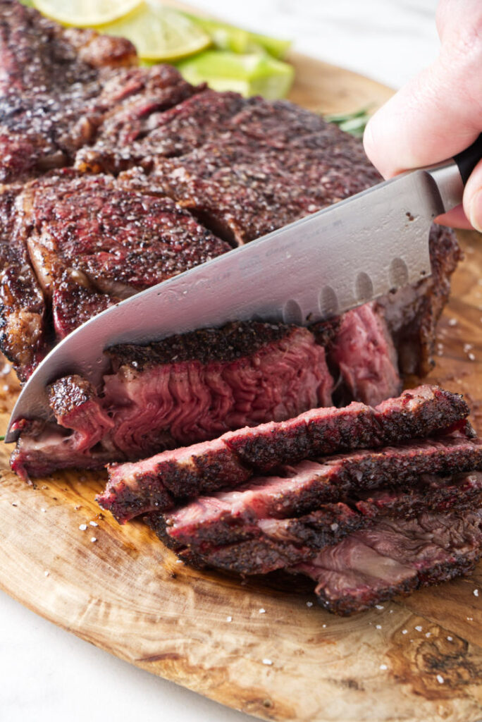 seared tomahawk steak being held vertically from the bone, resting on cutting board