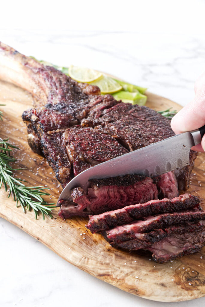 seared tomahawk steak being held vertically from the bone, resting on cutting board