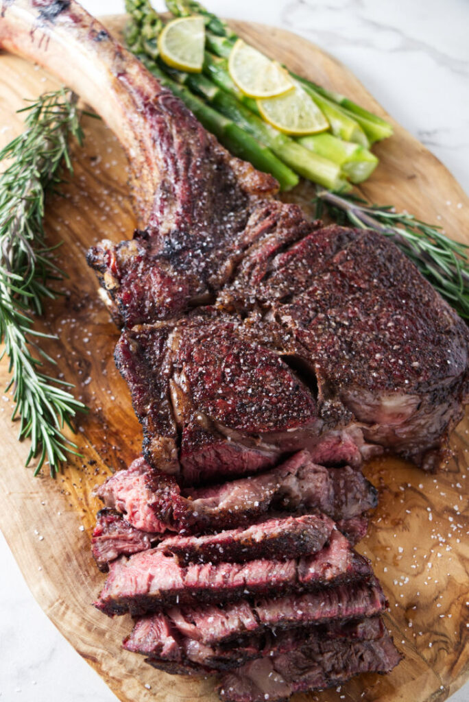 seared tomahawk steak being held vertically from the bone, resting on cutting board