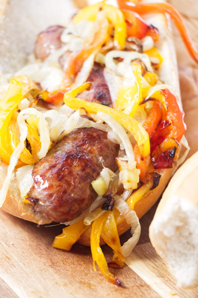 A bratwurst sandwich with onions, peppers, and cheese.