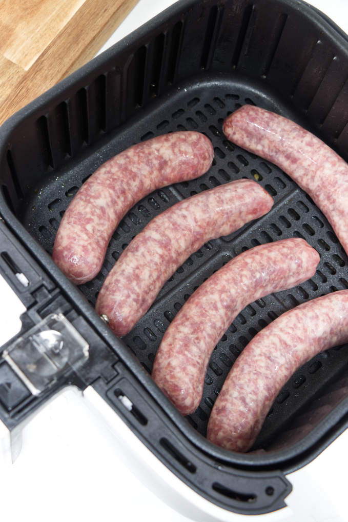 Five uncooked brats in an air fryer basket.
