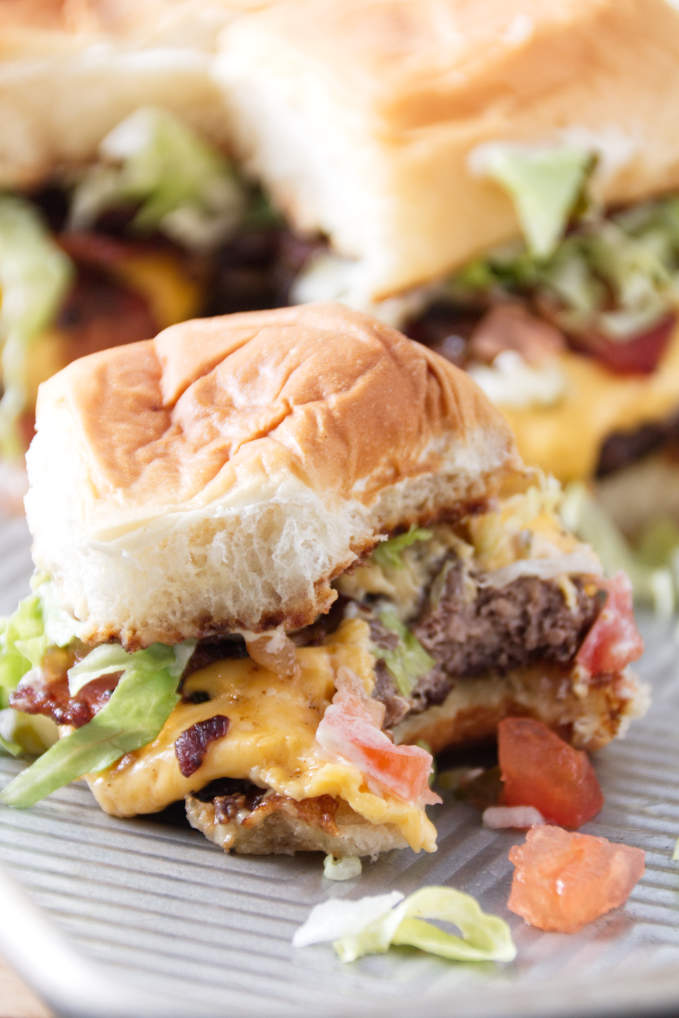 smashburger slider with a bit out of it, burger toppings spilling out onto sheet pan.