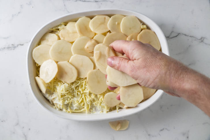 Adding a layer of sliced potatoes to a casserole dish.