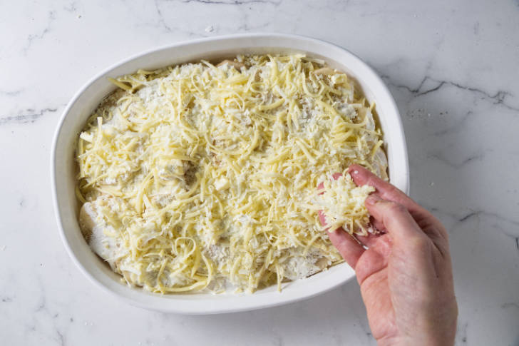 Sprinkling a layer of cheese on potatoes.