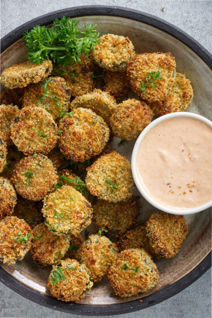 Air fried pickles on a platter with dipping sauce.