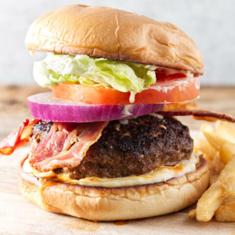 burger with bacon, onion, tomato, lettuce, and donkey sauce sitting on cutting board with fries