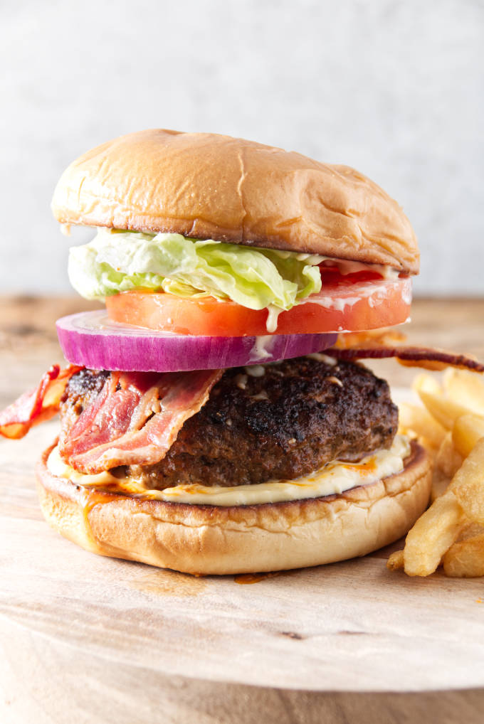 burger with bacon, onion, tomato, lettuce, and donkey sauce sitting on cutting board with fries