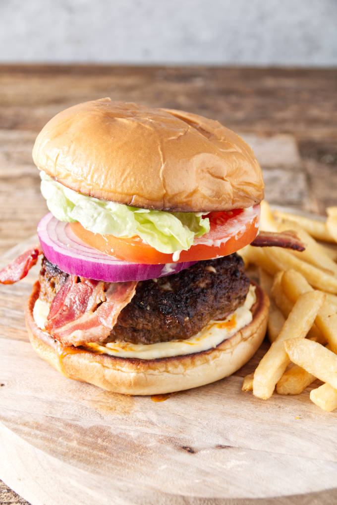 burger with bacon, onion, tomato, lettuce, and donkey sauce sitting on cutting board with fries