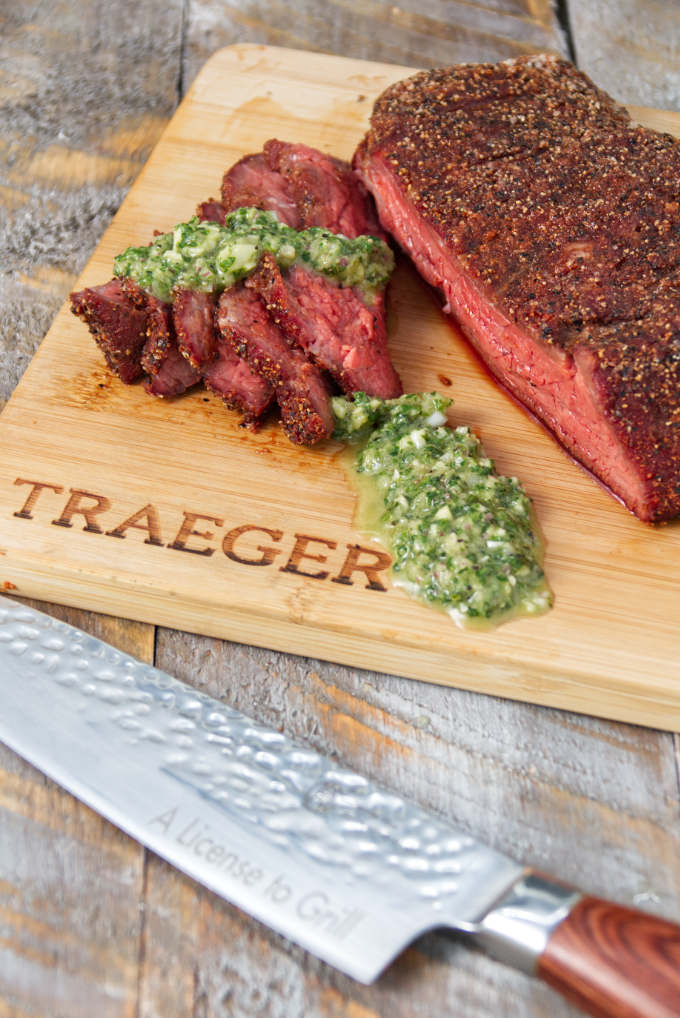 Traeger smoked tri-tip sliced on a cutting board topped with chimichurri