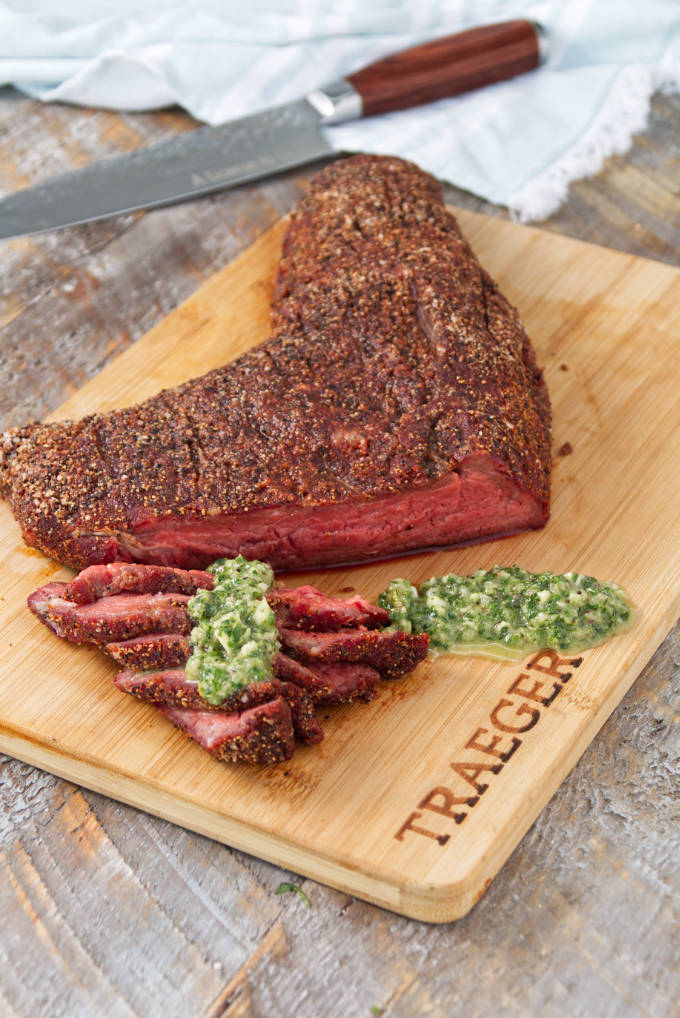 Traeger smoked tri-tip sliced on a cutting board topped with chimichurri