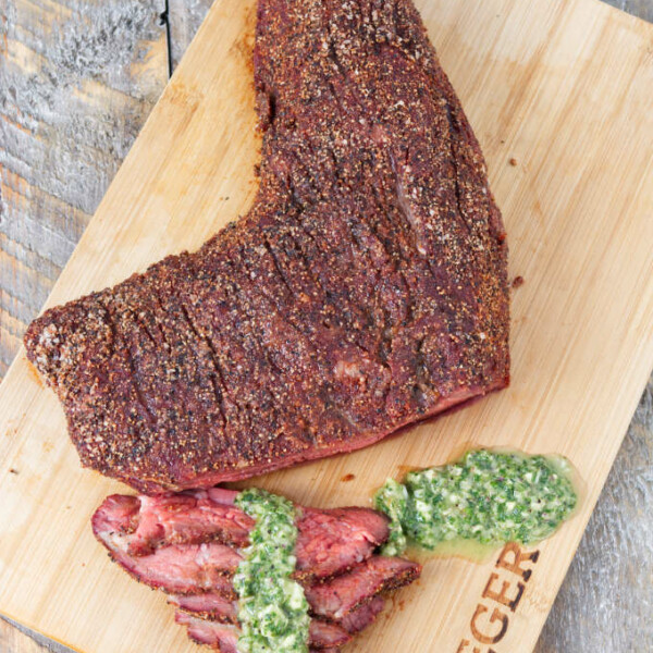 Traeger smoked tri-tip sliced on a cutting board topped with chimichurri